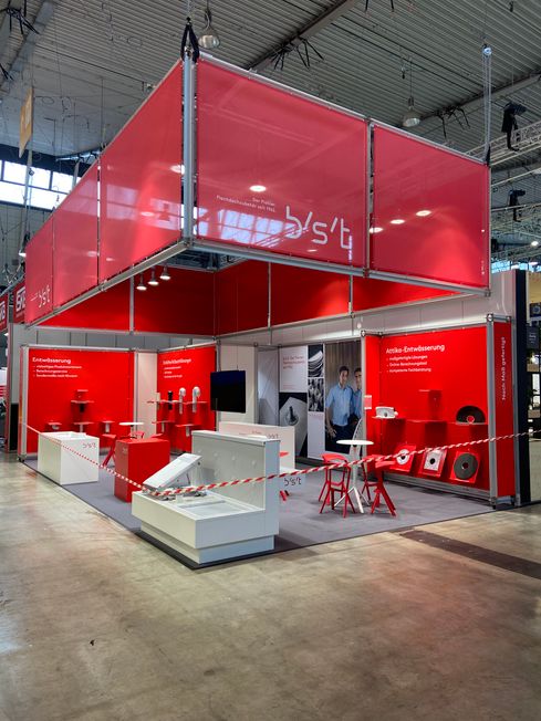Roter Messestand mit umlaufendem Fries und Produktpodesten