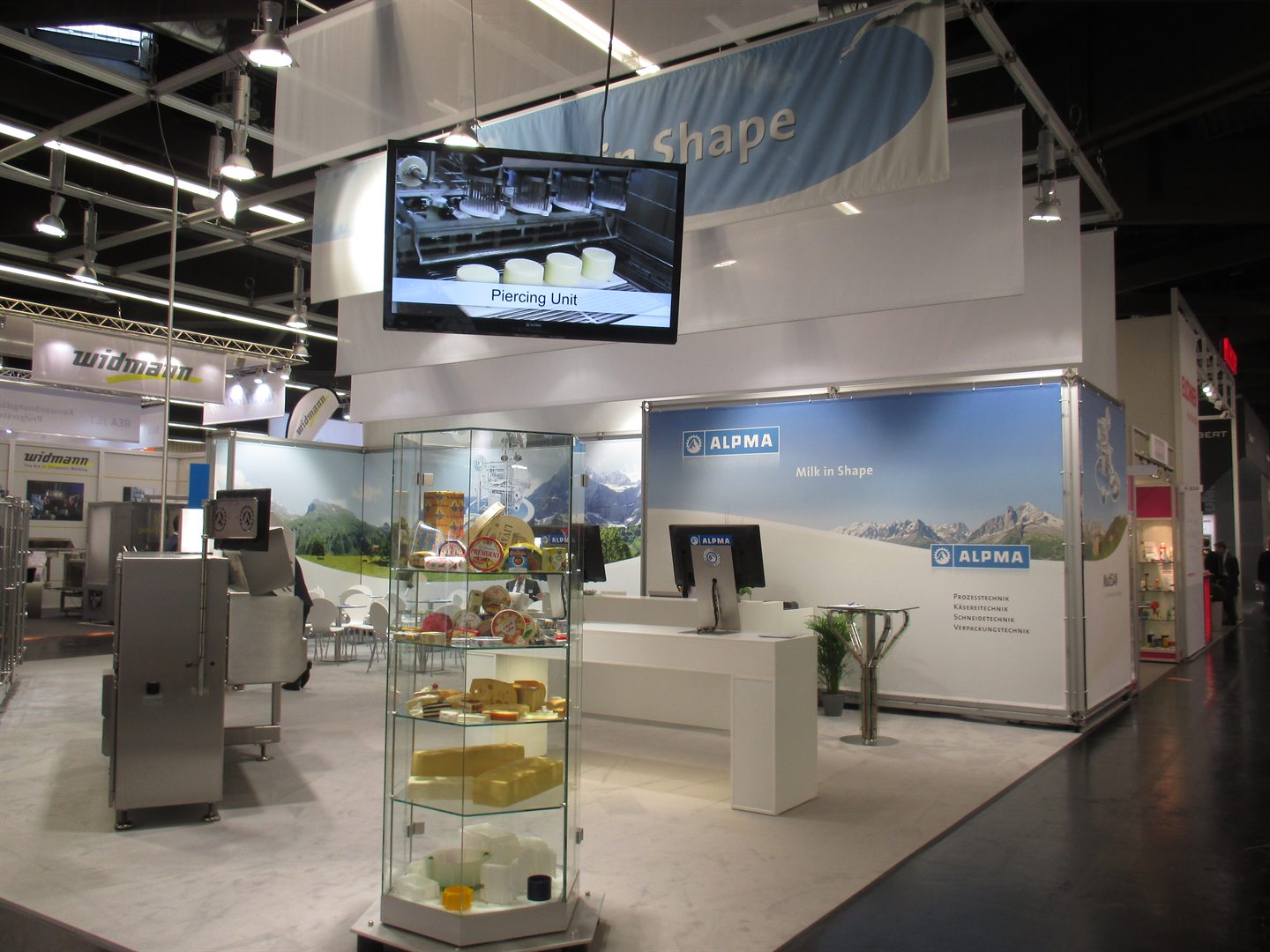 Messestand mit Alpenpanorama-Grafik, Glasvitrine und Maschinenexponat