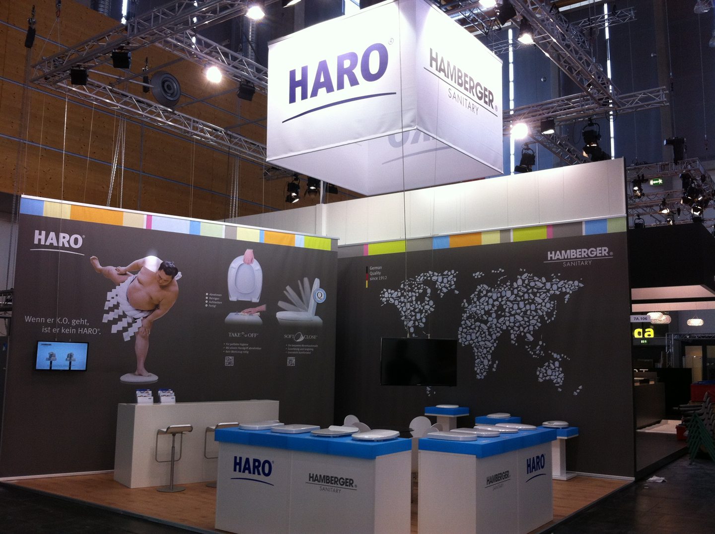 Messestand mit Weltkarten-Grafik, Leuchtkubus und Präsentationstischen für WC-Sitze