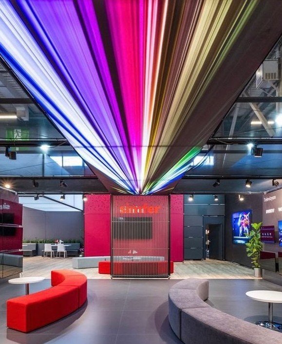 Messestand mit farbiger Lichtinstallation an der Decke und roten Loungemöbeln