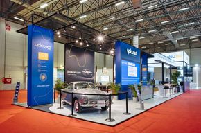 Messestand mit blauen Leuchtstelen und Oldtimer auf rotem Teppich